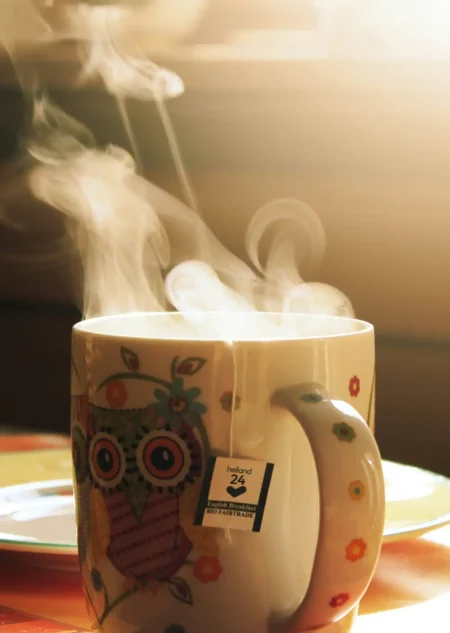 Bunte Tasse mit dampfendem Tee und heraushängendem Teebeutel im Sonnenlicht.